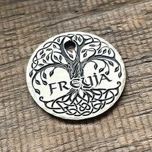 Load image into Gallery viewer, A silver round tag with a tree of life design engraved on it. The tree has a thick trunk and branches with leaves. The roots are intertwined and form a Celtic knot design. The name &#39;FREYJA&#39; is engraved in the center of the tag.