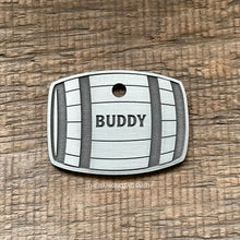Load image into Gallery viewer, hiskey Barrel shape Dog tag with 'Buddy' engraved on a wooden surface, branded 'The Barking Tagsmith'.