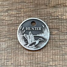 Load image into Gallery viewer, Dog ID tag with duck hunting scene deep engraved on round metal tag, personalised pet tag featuring flying duck, reeds and water design.
