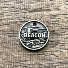 Load image into Gallery viewer, Personalised lighthouse dog ID tag with engraved ocean waves, coastal lighthouse and shoreline scene in brushed silver metal on rustic wood background