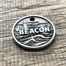 Load image into Gallery viewer, Personalised lighthouse dog ID tag with engraved ocean waves, coastal lighthouse and shoreline scene in brushed silver metal on rustic wood background