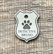 Load image into Gallery viewer, Dog ID tag shaped like a police badge with paw print design deep engraved on metal tag, personalised engraved pet tag reading Detective Bruno.