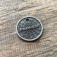 Load image into Gallery viewer, Personalised spider web dog ID tag with engraved gothic web pattern and raised Parker name in brushed silver metal on rustic wood background