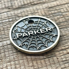 Load image into Gallery viewer, Personalised spider web dog ID tag with engraved gothic web pattern and raised Parker name in brushed silver metal on rustic wood background
